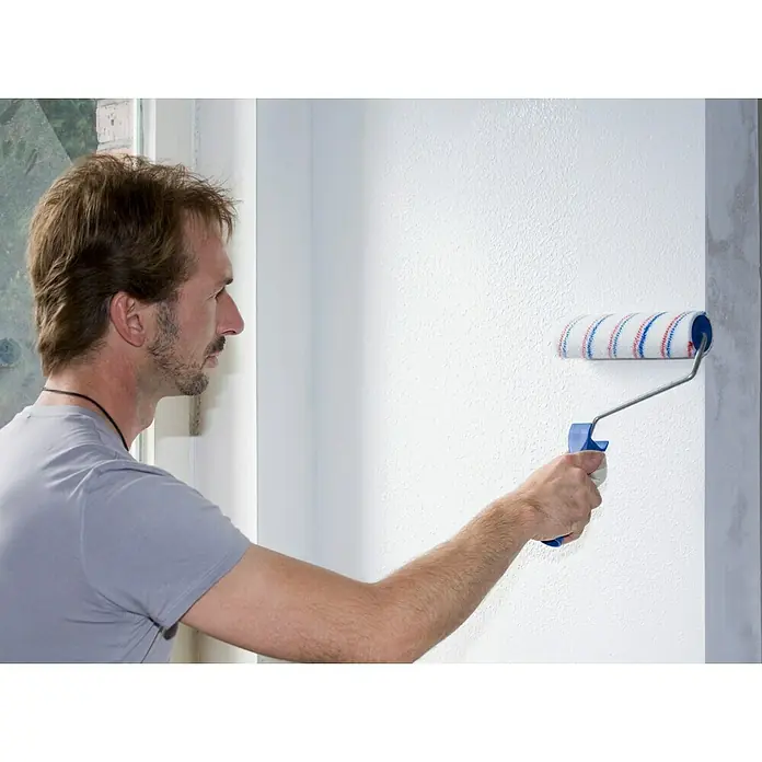 Knauf EasyPutz Dekoputz Extra fein - im Rezyklatgebinde - Weiß, Körnung: 0,5 mm, 20 kg, Konservierungsmittelfrei - Mann streicht eine Wand mit einer Farbwalze, die blaue und rote Streifen hat, wobei der Fokus auf der praktischen Anwendung der Walze liegt.