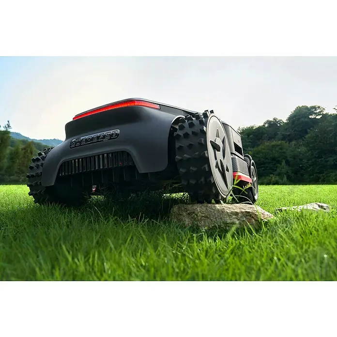 Dreame Mähroboter A3 AWD Pro 3500 - 3.500 m², Schnittbreite: 40 cm, Laser-gestützte Navigation, LiDAR - Ein dunkelgrauer Rasenroboter mit Stollenrädern und rotem Lichtstreifen, der Gras und einen Stein in einer Außenumgebung navigiert.