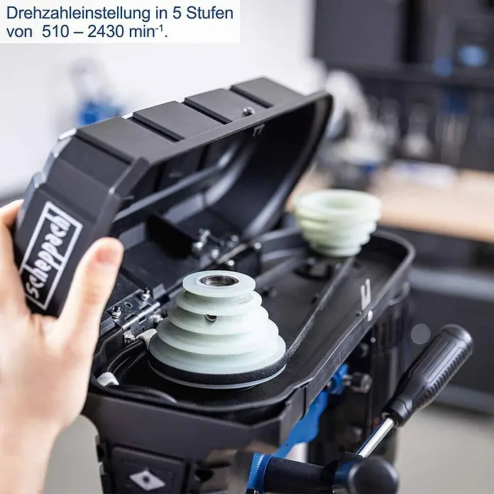 Scheppach Tischbohrmaschine TBM250 - 550 W, Leerlaufdrehzahl: 510 U/min - 2.430 U/min, Spannweite Bohrfutter: 1,5 mm - 13 mm - Bohrmaschine mit offenem schwarzem Deckel, der helle Stufenscheiben für 5-stufige Drehzahleinstellung von 510-2430 min⁻¹ zeigt.