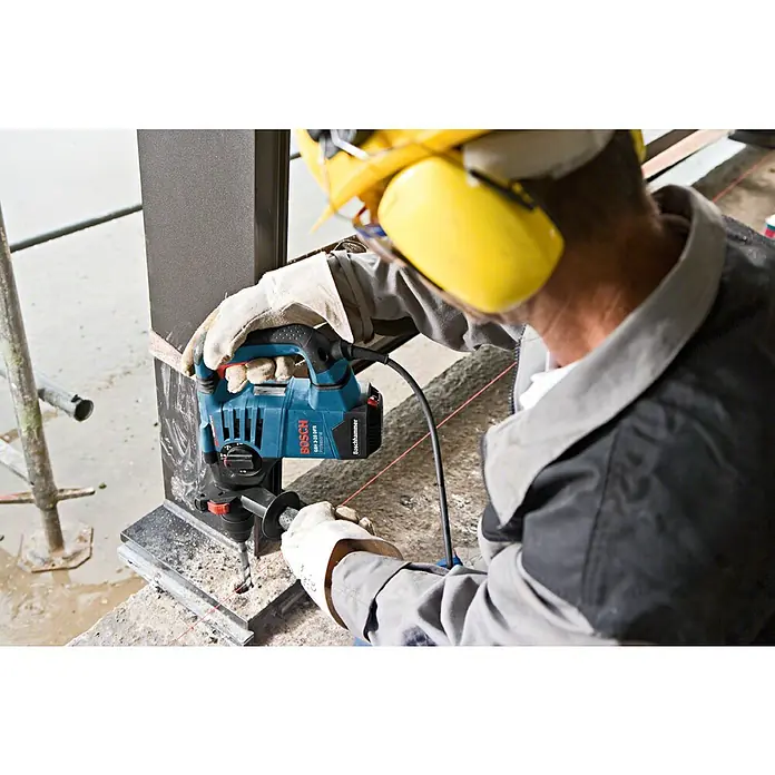 Bosch Professional Bohrhammer GBH 3-28 DFR - 800 W, 3,1 J, SDS-Plus-Aufnahme, Inkl. L-Boxx - Blaue Bosch Bohrhammer in Benutzung einer Person mit Schutzausrüstung, die in ein dunkles Strukturelement bohrt.