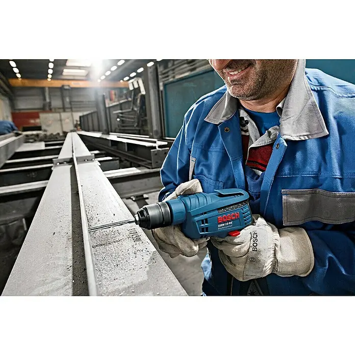 Bosch Professional Bohrmaschine GBM 10 RE - 600 W, ½″ Außenvierkant - Mann in Arbeitskleidung benutzt eine blaue Bosch GBM 10 RE Professional Bohrmaschine, um ein Loch in einen Metallträger zu bohren.