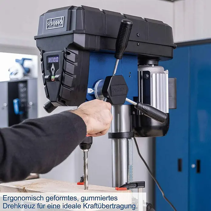 Scheppach Tischbohrmaschine TBM250 Vario - 600 W, Leerlaufdrehzahl: 1.490 U/min, Spannweite Bohrfutter: 3 mm - 13 mm - Eine Person bohrt mit einer blau-schwarzen Scheppach Standbohrmaschine. Sie hat eine Digitalanzeige und ein ergonomisches, gummiertes Drehkreuz.