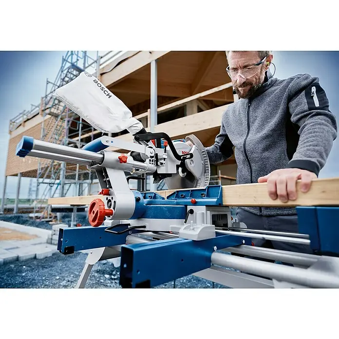 Bosch Professional AMPShare 18V Akku-Kapp- & Gehrungssäge GCM 18V-254 D - 18 V, Ohne Akku, 4.500 U/min - Blaue und silberne Bosch Gehrungssäge, von einem Mann zum Sägen eines Holzbretts auf einer Baustelle verwendet.
