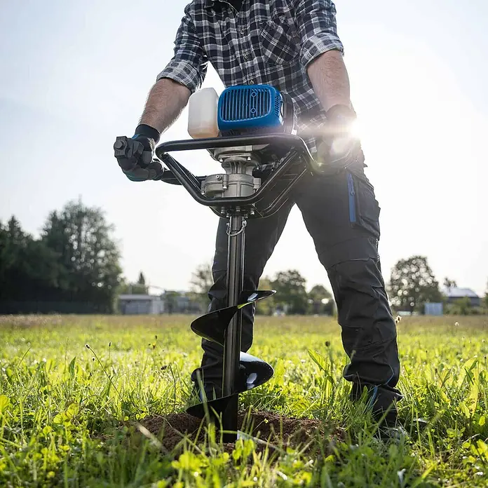 Scheppach Erdbohrer EB2000 - 1.450 W, Durchmesser Bohrer: 100 mm - Mann bedient einen blau-schwarzen Erdbohrer, um ein Loch in einem Grasfeld zu bohren.