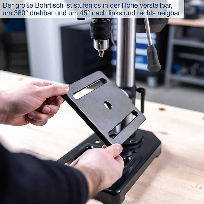 Scheppach Tischbohrmaschine TBM200 - 400 W, 550 U/min - 2.600 U/min, Spannweite Bohrfutter: 1,5 mm - 13 mm - Hände halten einen schwarzen Bohrtisch aus Metall mit mittigem Loch und Schlitzen. Er ist höhenverstellbar, 360° drehbar und 45° neigbar.