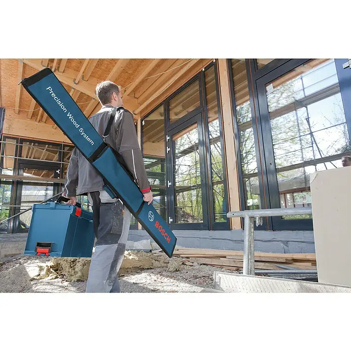 Bosch Professional Transporttasche FSN - 550 x 224 x 70 mm - Mann trägt eine blaue Bosch 'Precision Wood System' Werkzeugtasche und einen blauen Bosch Werkzeugkoffer auf einer Baustelle.