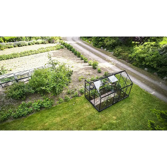 Halls Gewächshaus Popular 106 - Außenmaß inkl. Dachüberstand (B x T): 193 x 319 cm, Blankglas, 3 mm, Schwarz - Ein Gewächshaus mit schwarzem Rahmen in einem Garten, gefüllt mit üppigen Pflanzen, von oben gesehen.
