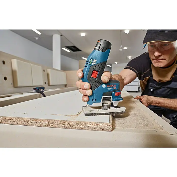 Bosch Professional Akku-Kantenfräser GKF 12V-8 PRO - 2 Akkus, 12 V - Bosch Professional GKF 12V-8 Kantenfräser (blau/schwarz) bearbeitet die Kante einer hellen Holzplatte.