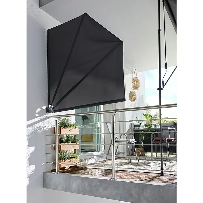 Sunfun Balkonfächer - Anthrazit, 1,4 x 1,4 m - Schwarze fächerförmige Balkonmarkise an einer weißen Wand, spendet Schatten über einem Balkon mit Pflanzen und Möbeln.