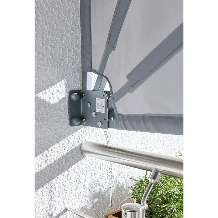 Sunfun Balkonfächer - Grau, 1,4 x 1,4 m - Nahaufnahme eines wandmontierten grauen Sonnenschutzes mit Metallhalterung an einer strukturierten Wand über einem Metallgeländer und Grünpflanzen.