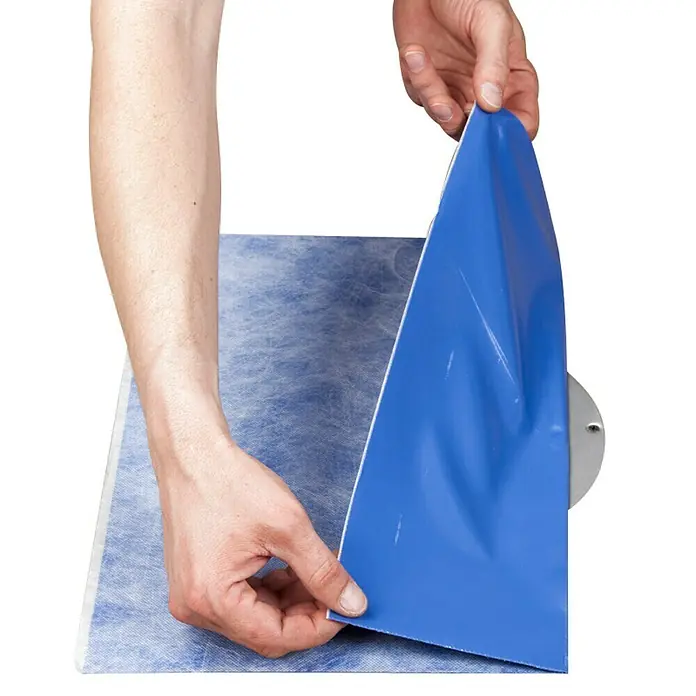 Knauf Butyl-Dichtmanschette - 1 Stk., 370 x 370 mm - Nahaufnahme einer Person, die eine blaue selbstklebende Antirutschmatte auf einem Untergrund befestigt. Die Matte ist eine Sicherheitsvorrichtung.