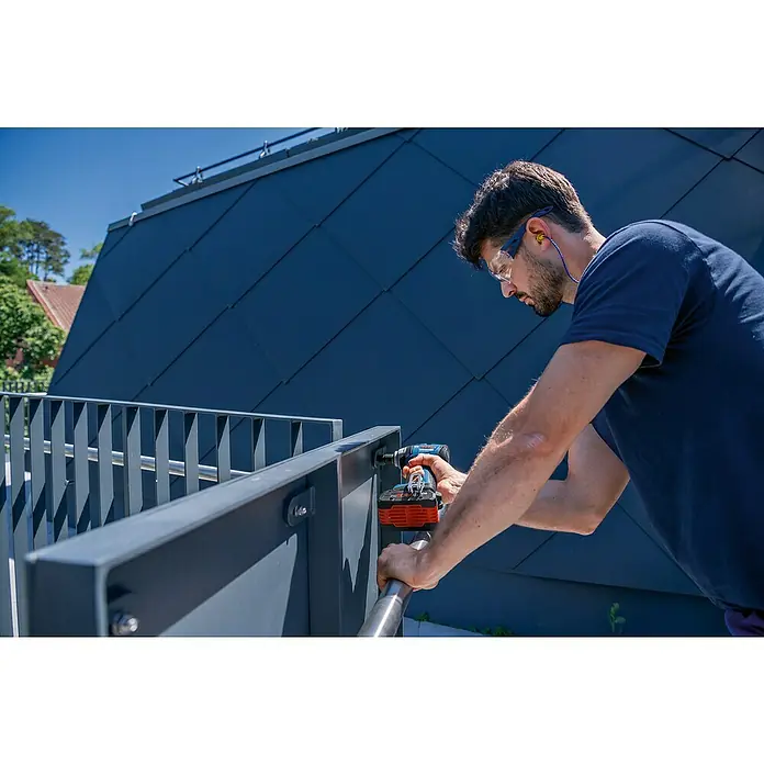 Bosch Professional AMPShare 18V Akku-Drehschlagschrauber GDS 18V-330 HC - 18 V, 330 Nm, 2 x Akku GBA 18V 5.0Ah - Dunkelgraues Metallgeländer wird von einem Arbeiter mit einem Bohrer montiert.