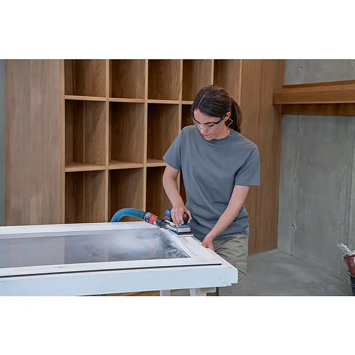 Bosch Professional Akku-Schwingschleifer GSS 12V-13 PRO - Ohne Akku, 12 V - Blauer Exzenterschleifer mit Staubabsaugung wird von einer Frau zum Schleifen eines weißen Holzrahmens benutzt. Sie trägt Schutzausrüstung.