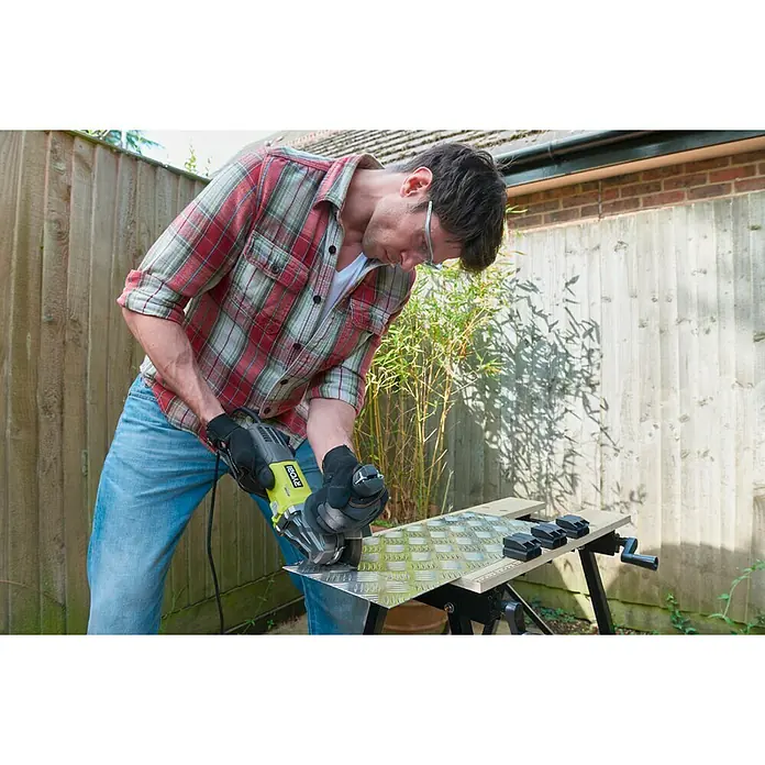 Ryobi Amoladora angular eléctrica RAG800-125G - 800 W, Diámetro disco: 125 mm, Número de revoluciones de marcha en vacío: 12.000 r.p.m. - Hombre cortando metal con una amoladora angular Ryobi, usando gafas de seguridad y guantes protectores.