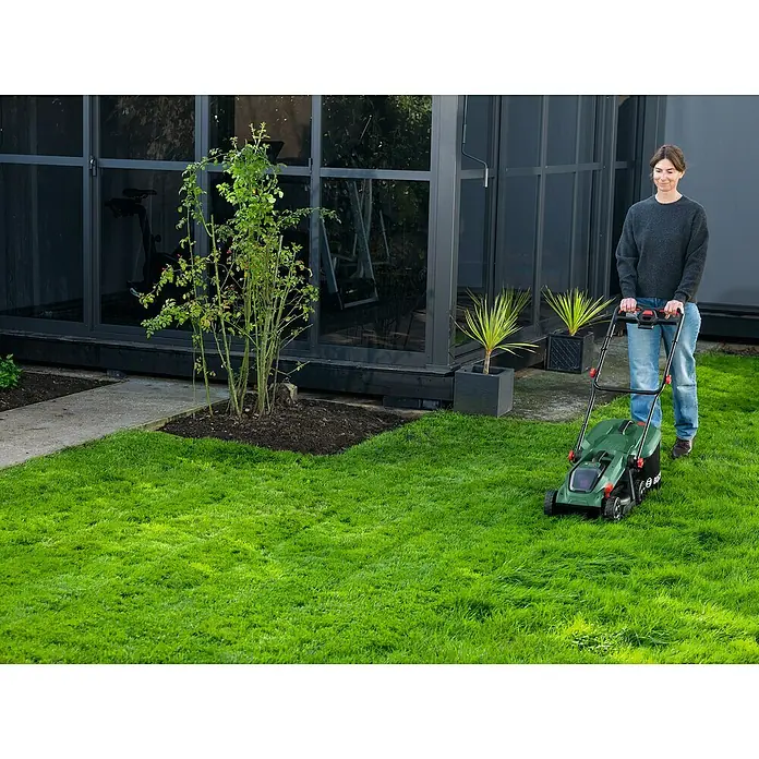 Bosch Power for All 18V Akku-Rasenmäher ROTAK18V-32 - Ohne Akku, Schnittbreite: 32 cm - Grüner Rasenmäher, von einer Frau auf einem Rasen bedient.