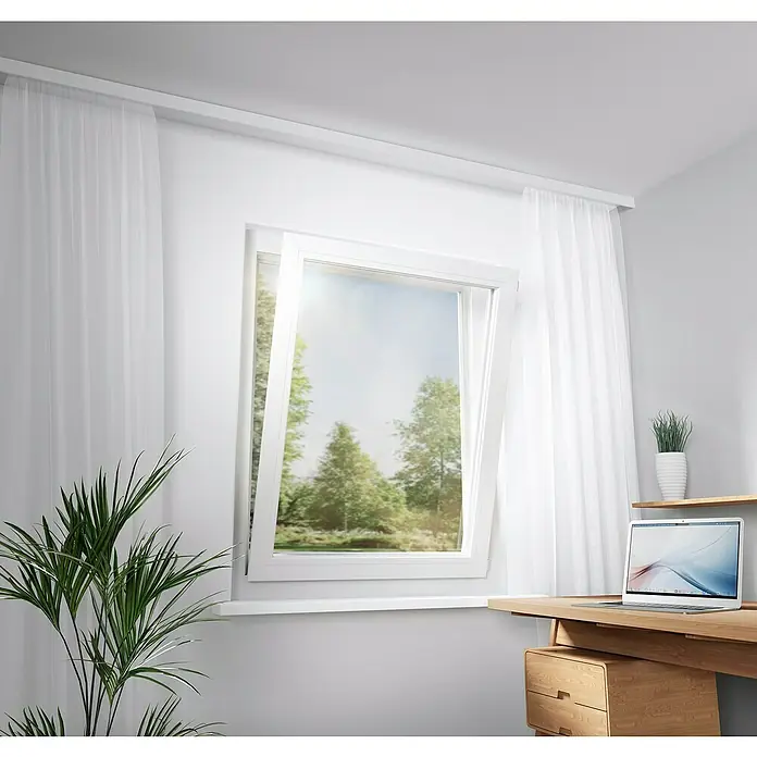 Tesa Sonnen-& Insektenschutz-Gitter - B x H: 130 x 150 cm, Montage Insektengitter: Ankletten - Heller Raum mit offenem Kippfenster, transparenten weißen Vorhängen und einem Schreibtisch mit Laptop, Blick auf grüne Bäume.