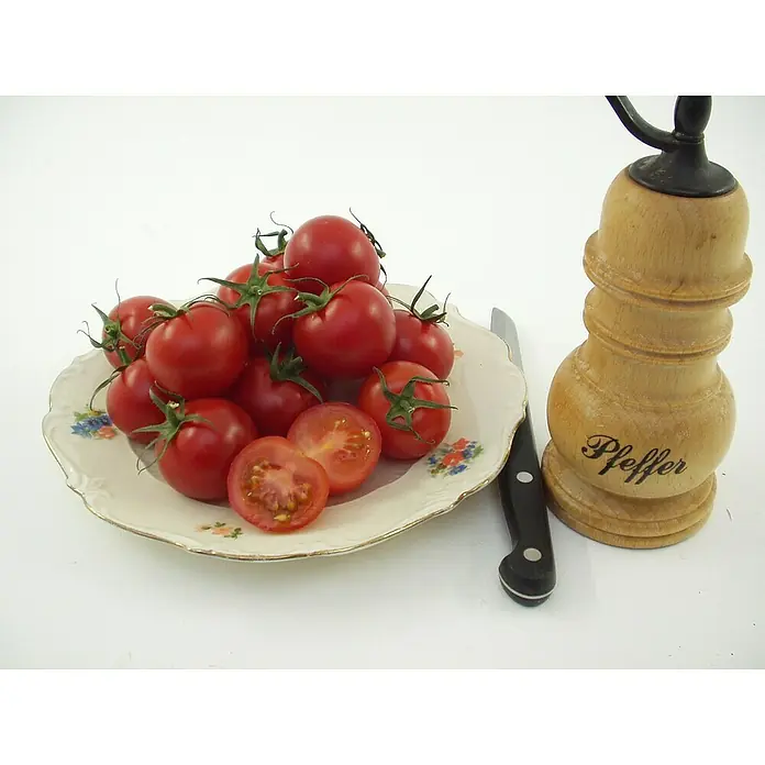 Blu Bio Mini-Tomate - Lycopersicon esculentum, 12 cm, Erntezeit: Juli - Rote Kirschtomaten auf einem Teller, ein Messer und eine hölzerne Pfeffermühle mit der Aufschrift „Pfeffer“.
