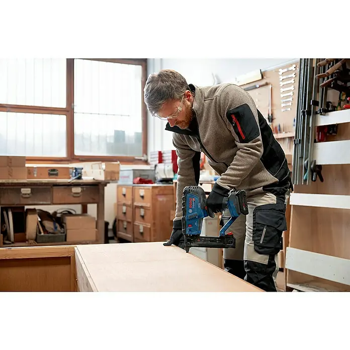 Bosch Professional Akku-Tacker GTH 18V-38 M PRO SOLO - 18 V, Ohne Akku, Klammertiefe: 10 mm - 38 mm - Mann verwendet eine blau-schwarze Bosch Akku-Nagelpistole zum Befestigen von Holz in einer Werkstatt.