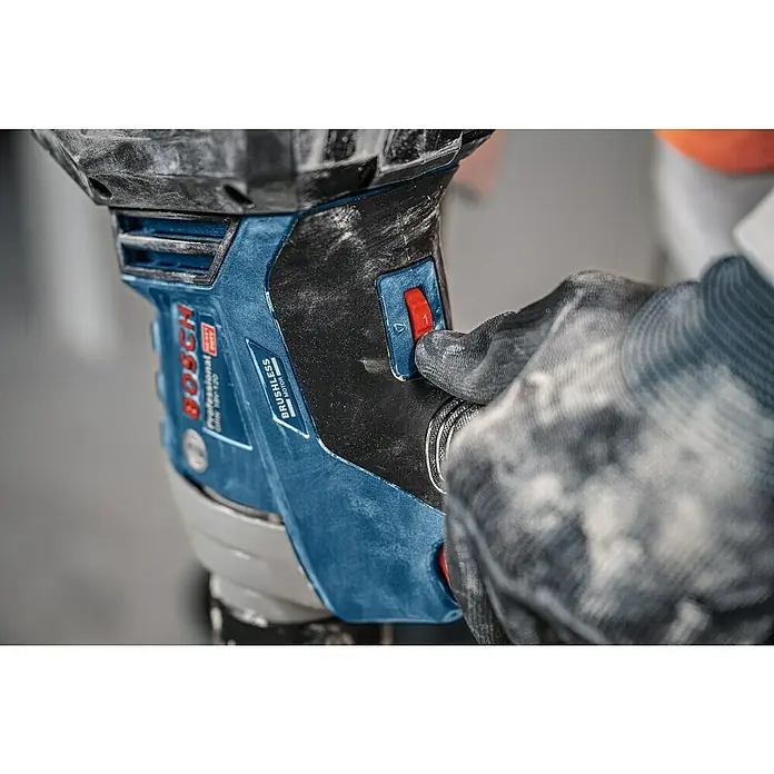 Bosch Professional Akku-Rührwerk GRW 18V-120 - 18 V, Anzahl Akkus: Ohne Akku - Nahaufnahme einer behandschuhten Hand, die den roten Schalter eines staubigen blau-schwarzen Bosch Professional Akkugeräts drückt.