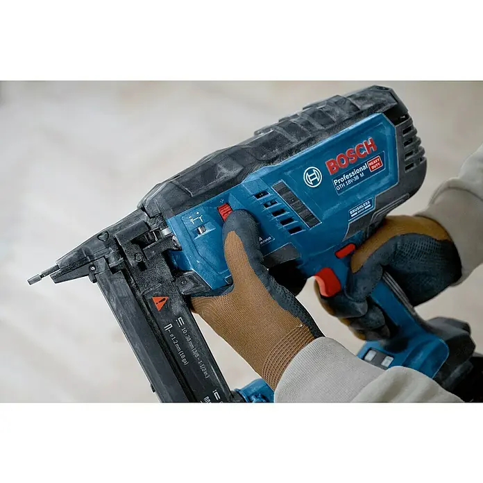 Bosch Professional Akku-Tacker GTH 18V-38 M PRO SOLO - 18 V, Ohne Akku, Klammertiefe: 10 mm - 38 mm - Eine behandschuhte Hand hält einen blau-schwarzen Bosch Professional GTH 18V-38 M Akku-Nagler/Tacker. Das Magazin zeigt Nagel-/Klammergrößen.