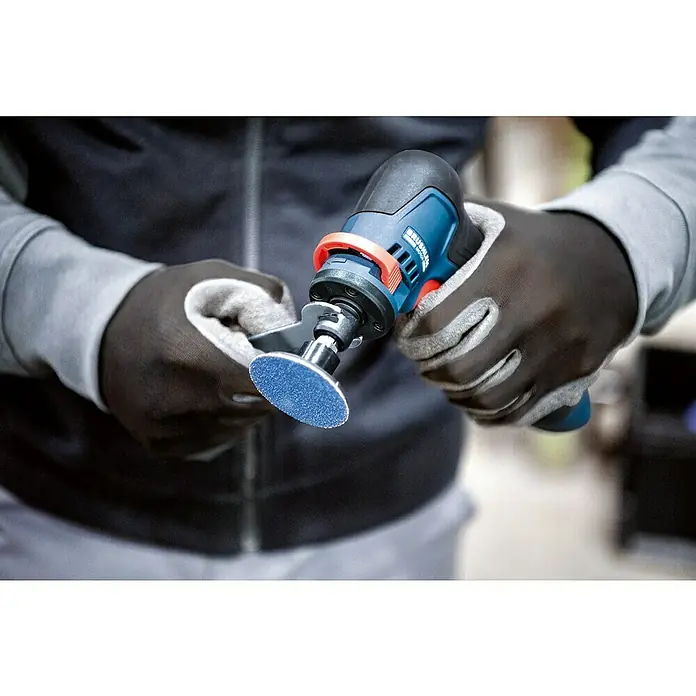 Bosch Professional Geradschleifer GWG 12V-50 S PRO SOLO - Leerlaufdrehzahl: 5.000 U/min - 15.000 U/min - Eine Person in Arbeitshandschuhen hält ein blau-schwarzes kompaktes Rotationswerkzeug mit einer kleinen blauen Schleifscheibe.