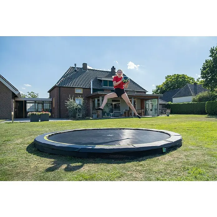 Exit Toys Trampolin Silhouette Sports - Durchmesser: 366 cm, Schwarz - Ein Mädchen springt auf einem schwarzen, runden Bodentrampolin mit gelb-grünem Sicherheitsrand im sonnigen Garten.