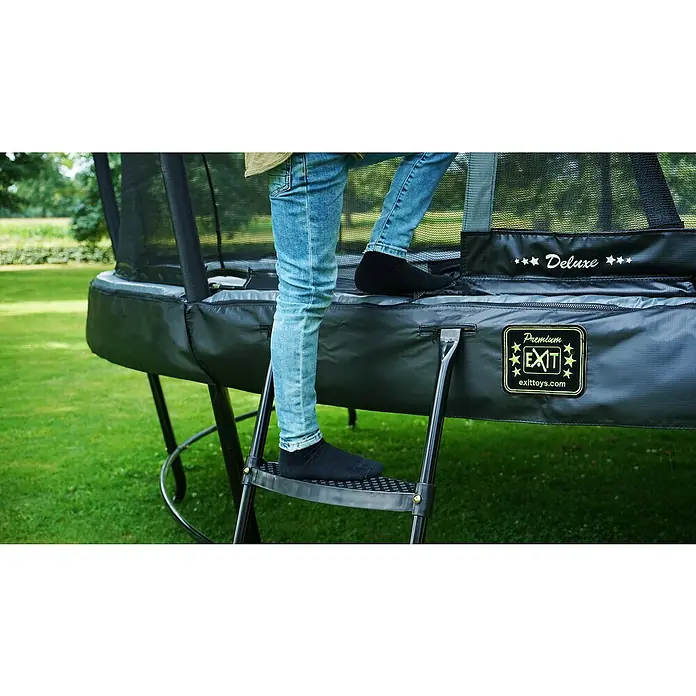 Exit Toys Trampolin-Leiter - Stahl, Schwarz, Passend für: Rahmenhöhe 80 - 95 cm - Person steigt über schwarze Leiter auf dunkelgraues Trampolin, mit 'Deluxe' und 'Premium EXIT' Logos.