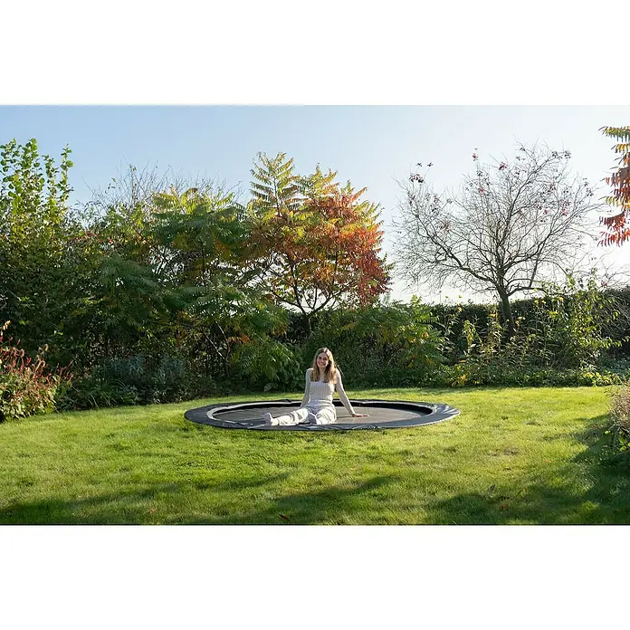 Exit Toys Trampolin Interra Sports - Durchmesser: 244 cm, Ebenerdig, Schwarz - Schwarzes und graues Bodentrampolin, auf dem eine junge Frau sitzt.