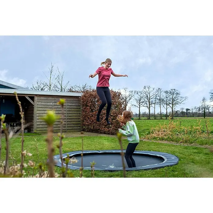 Exit Toys Trampolin Interra Sports - Durchmesser: 244 cm, Ebenerdig, Schwarz - Zwei Mädchen springen auf einem runden, dunkelgrauen Trampolin mit hellgrauem Schutzrand.