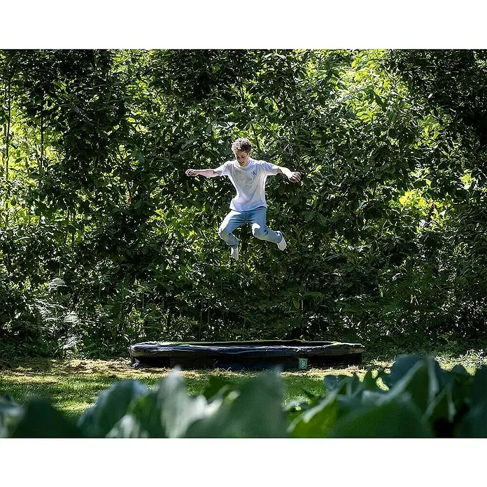 Exit Toys Trampolin Silhouette Sports - Durchmesser: 244 cm, Schwarz - Rundes schwarz-grünes Trampolin in einem Garten, auf dem ein Junge springt.