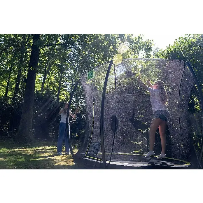 Exit Toys Trampolin Silhouette Bodentrampolin mit Sicherheitsnetz - Durchmesser: 305 cm, Rosa - Zwei Mädchen spielen mit einem schwarzen Trampolin und Sicherheitsnetz draußen; eines springt drinnen und fängt einen Ball.
