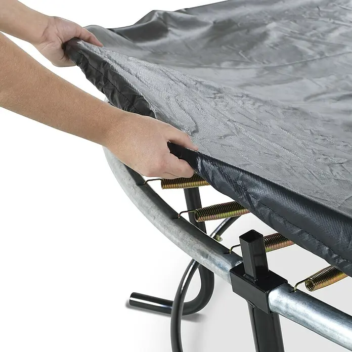 Exit Toys Trampolin-Abdeckplane Premium - Durchmesser: 427 cm, Schwarz, Kunststoff - Hände legen eine schwarze Schutzabdeckung über den Metallrahmen und die Federn eines Trampolins.