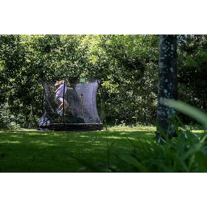 Exit Toys Trampolin Silhouette Bodentrampolin mit Sicherheitsnetz - Durchmesser: 305 cm, Rosa - Ein Kind springt hoch auf einem schwarzen Trampolin mit Sicherheitsnetz und grünen Akzenten in einem sonnigen Garten.