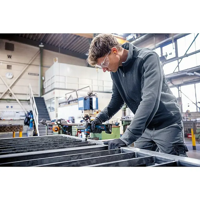 Bosch Professional Akku-Geradschleifer GWG 12V-50 S PRO SOLO - 12 V, Leerlaufdrehzahl: 5.000 U/min - 15.000 U/min - Person in einer Werkstatt, die ein blau-schwarzes Bosch Akku-Rotationswerkzeug zum Bearbeiten von Metallstangen verwendet.
