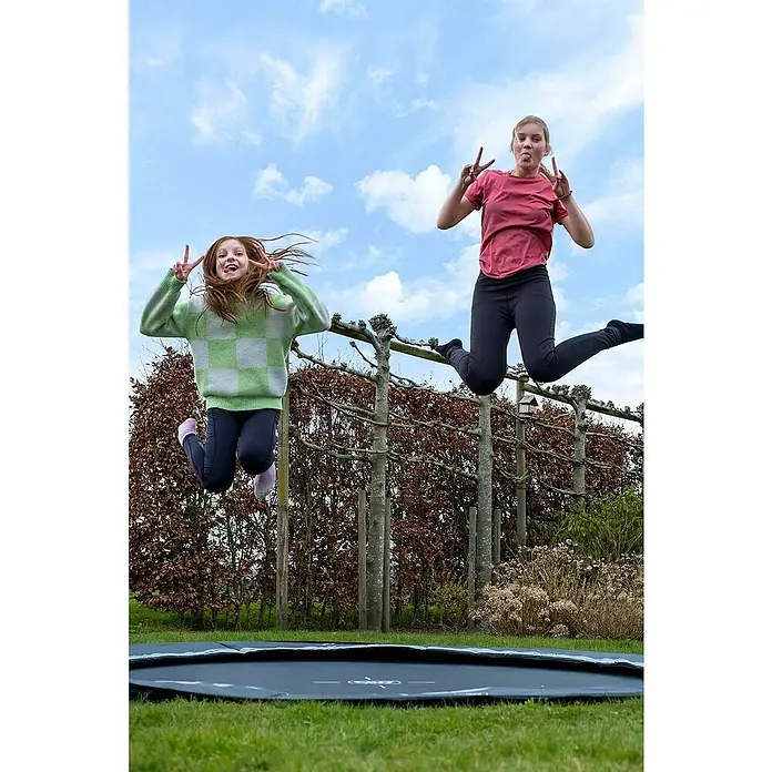 Exit Toys Trampolin Interra Sports - Durchmesser: 244 cm, Ebenerdig, Schwarz - Zwei Mädchen springen hoch auf einem schwarzen Bodentrampolin im grünen Gras.
