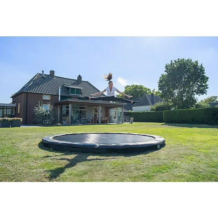 Exit Toys Trampolin Silhouette Sports - Durchmesser: 427 cm, Schwarz - Ein Mädchen springt hoch auf einem runden, schwarzen Bodentrampolin in einem sonnigen grünen Garten.