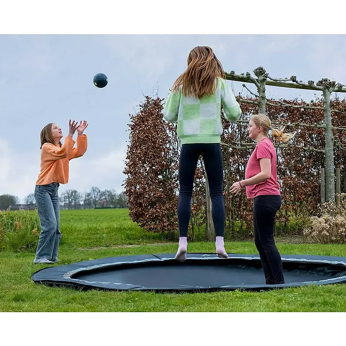 Exit Toys Trampolin Interra Sports - Durchmesser: 244 cm, Ebenerdig, Schwarz - Drei Kinder spielen auf einem schwarzen Bodentrampolin mit blauem Streifenrand in einem Garten.