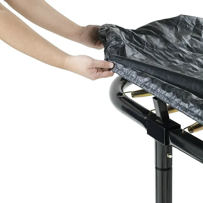 Exit Toys Trampolin-Abdeckplane Premium - 305 x 519 cm, Schwarz - Hände legen eine schwarze, texturierte Trampolinabdeckung über einen Trampolinrahmen mit Federn.