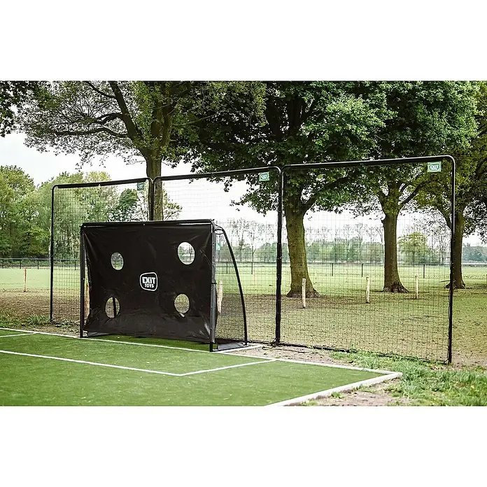 Exit Toys Sportnetz Backstop - 900 x 300 cm, Schwarz - Schwarzes Fußballtor mit Zielplane auf Kunstrasen, neben einem Zaun.
