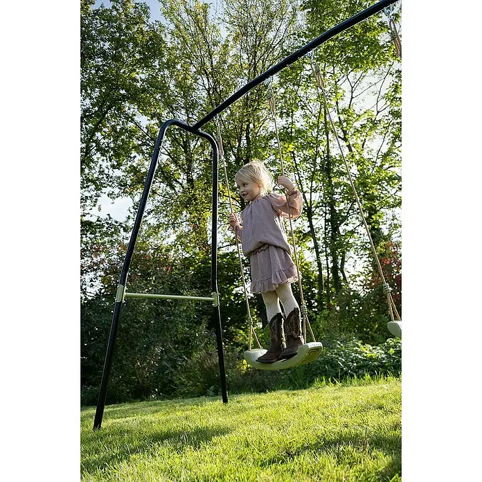Exit Toys Schaukel Ivy - B x L: 243 x 110 cm, Metall - Ein kleines Kind steht auf einer grünen Schaukel eines schwarzen Metallschaukelgerüsts in einem sonnigen Garten.