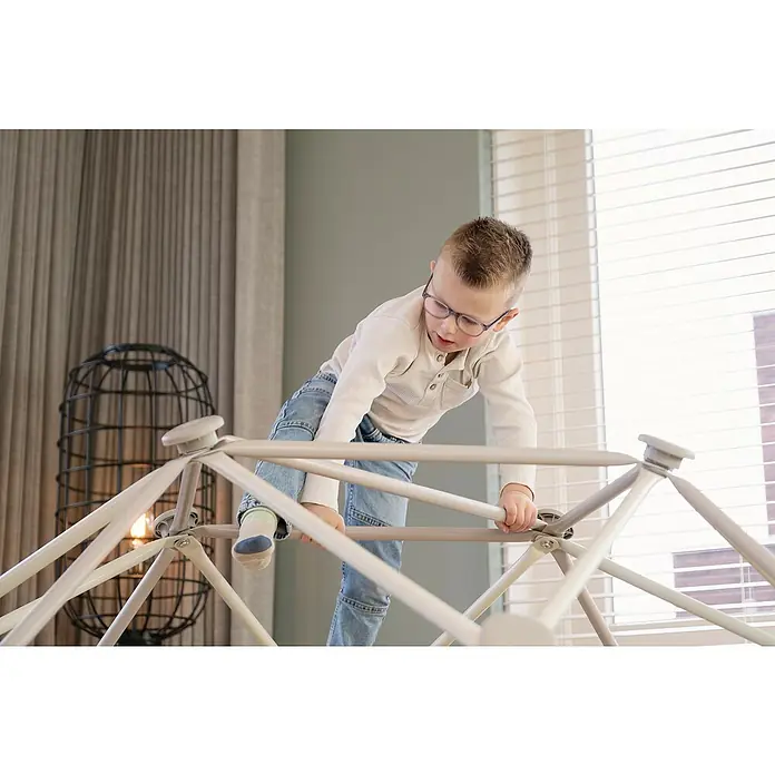 Exit Toys Klettergerüst Climbing Dome - Ø x H: 190 x 92 cm, Stahl, Pastell - Kind in Brille und Jeans spielt auf einem hellen Klettergerüst in Geodätischer Kuppel drinnen.
