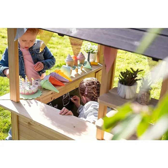Exit Toys Spielhaus Hika - L x B x H: 140 x 111 x 155 cm, Holz, Natur - Zwei Kinder spielen an einem Marktstand aus Naturholz im Freien mit Spielzeug-Eis, Kuchen und einer Kreidetafel.