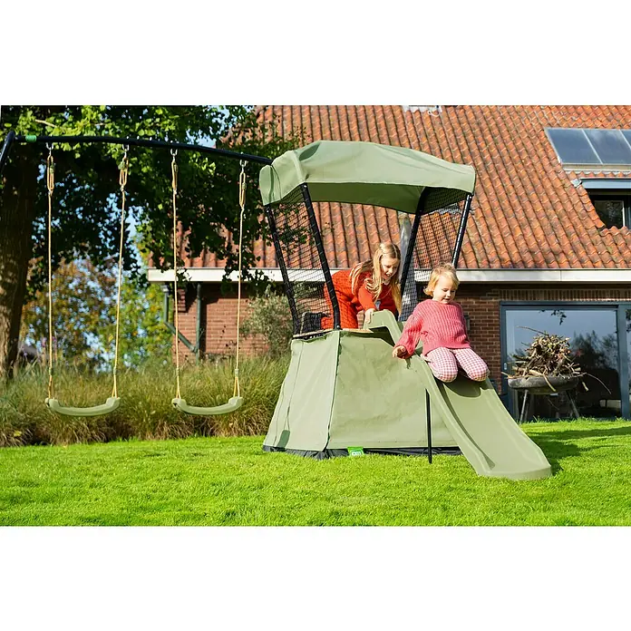 Exit Toys Spielhaus Ivy - L x B x H: 253 x 340 x 216 cm, Holz, Grün/Schwarz, Mit Rutsche und Doppelschaukel - Zwei Kinder spielen auf einer grünen Outdoor-Schaukel und einem Spielhaus mit Rutsche im Garten.