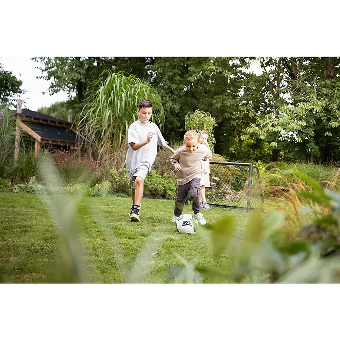 Exit Toys Fußballtor Scala - 120 x 55 x 80 cm, Schwarz - Drei Kinder spielen Fußball im Garten. Ein Junge dribbelt den Ball auf ein kleines Tor.