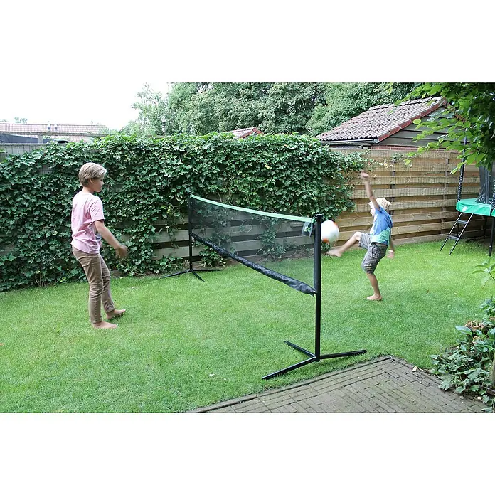 Exit Toys Sportnetz - Höhenverstellbar, 300 x 155 cm, Stahl - Tragbares schwarzes Sportnetz mit grünem Rand in einem Garten. Zwei Jungen spielen Ball, einer tritt einen Ball über das Netz.