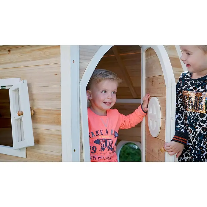 Exit Toys Spielhaus Fantasia 100 - L x B x H: 128 x 108 x 171 cm, Holz, Natur - Zwei fröhliche Kinder spielen in einem hölzernen Spielhaus mit weißer Verzierung.