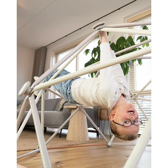 Exit Toys Klettergerüst Climbing Dome - Ø x H: 190 x 92 cm, Stahl, Pastell - Kind hängt kopfüber an einem hellen Indoor-Klettergerüst mit mehreren Stangen und lächelt.