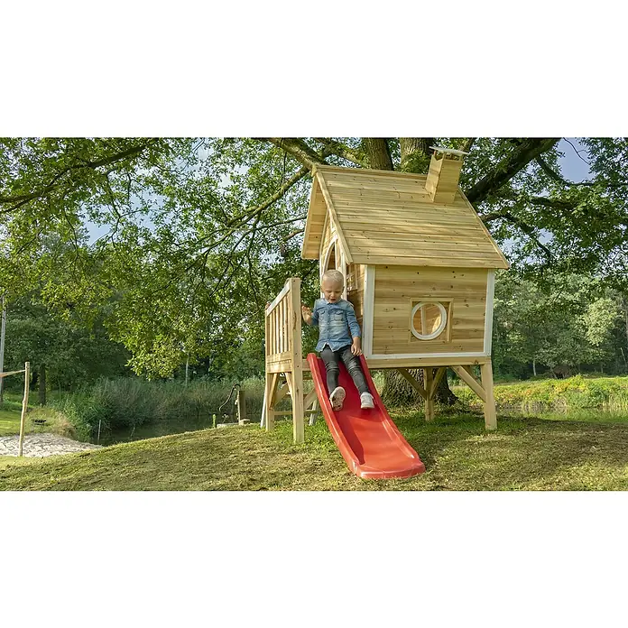 Exit Toys Spielhaus Fantasia 300 - L x B x H: 246 x 166 x 227 cm, Holz, Rot - Holzspielhaus mit roter Rutsche, auf der ein Kind draußen spielt.