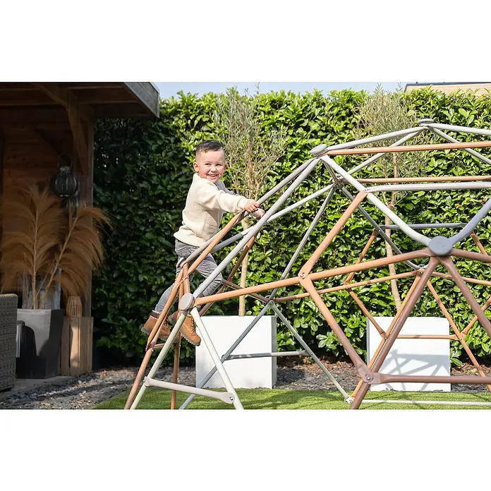 Exit Toys Klettergerüst Climbing Dome - Ø x H: 300 x 165 cm, Stahl, Pastell - Glücklicher kleiner Junge klettert auf einer geodätischen Kuppel aus grauen und braunen Metallstangen.