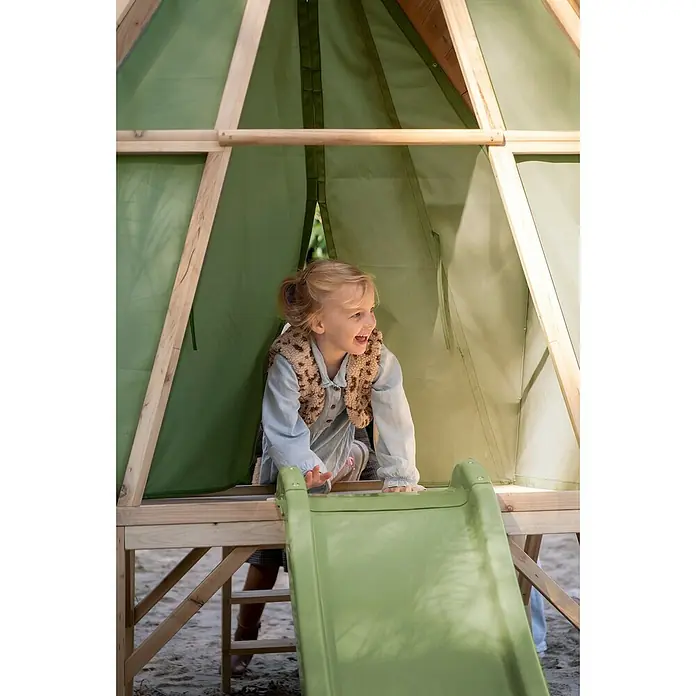 Exit Toys Spielhaus Yuki 350 - L x B x H: 256 x 148 x 219 cm, Holz, Natur/Grün - Ein lächelndes Kind kommt aus einem Holzspielhaus mit grüner Stoffabdeckung und bereitet sich vor, eine grüne Rutsche hinunterzugehen.